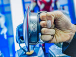 Hand holding the shield speaker by the strap, control buttons visible